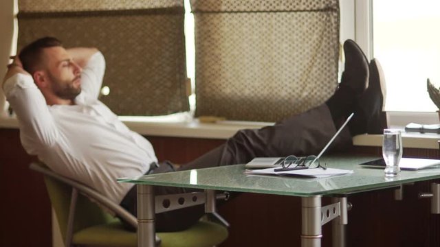 Boss day. Office hierarchy, supervisor. Mature male businessman in white shirt throws his legs on the table. Rest time, break in work, coffee break