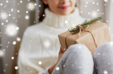 childhood, winter holidays and people concept - happy beautiful girl with christmas gift sitting on sill at home window