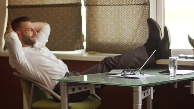 Boss day. Office hierarchy, supervisor. Young confident male businessman in white shirt and glasses throws his legs on the table. Rest time, break in work, coffee break