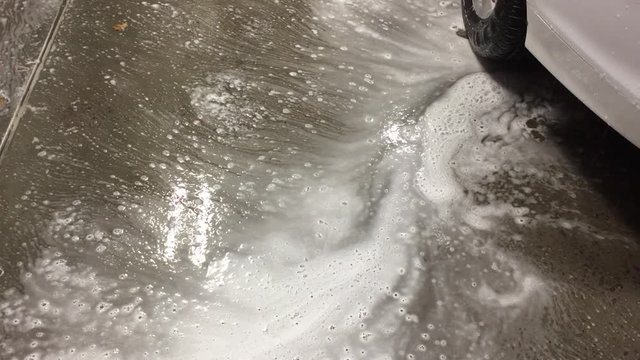 Dirty foam flows down the drain at a car wash.