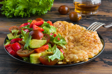 Tilapia fish fillet baked with grated cheese and paprika topping and vegetable salad. Blake plate, wooden table.
