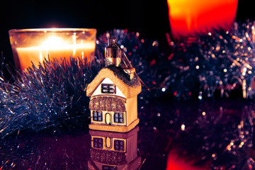 Fototapeta premium Colorful snow-covered houses with romantic reflections and Christmas candles atmospheric lights on a blurred background with bokeh effect. Christmas and New Year holiday background concept.