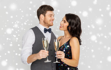 christmas party, new year celebration and holidays concept - happy couple with glasses drinking non alcoholic champagne over grey background and snow