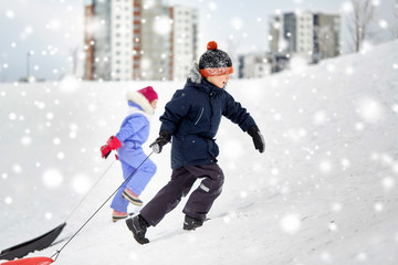 Fototapeta na wymiar childhood, sledging and season concept - happy little kids with sleds climbing snow hill in winter