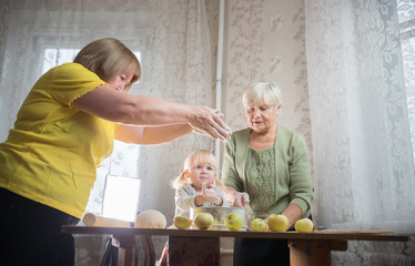 Two elderly woman making apple little pies at home. Sifting flour with little girl.