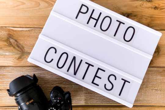 Text "photo contest"  written on white slate with camera on wooden background. Suitable for advertising