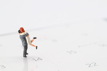 Miniature people: a couple standing on calendar at 14 February , meaning of love.