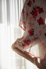 Beautiful girl model standing at the window in see trough kimono and playing with her legs