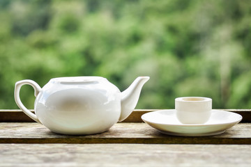 White porcelain teapot and cup on wooden deck by green tea plantation garden background. Fresh green tea is very healthy.
