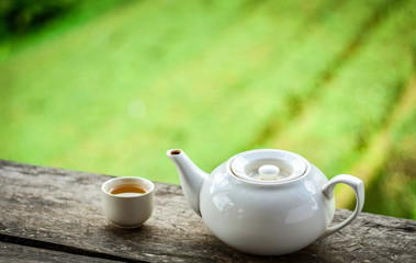 White ceramic teapot and cup on wooden deck by green tea plantation garden background. Fresh green tea is very healthy.
