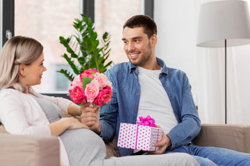 holidays, pregnancy and greetings concept - happy man giving flowers to pregnant woman at home