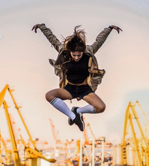 Outdoor lifestyle image of a young pretty chestnut haired caucasian girl having fun, jumping and...
