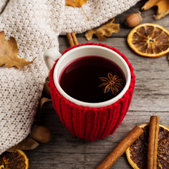 Mulled wine in a cup in a case. Leaves, knitted plaid, dry orange, cinnamon and acorns on the old wooden table, copy space, autumn.