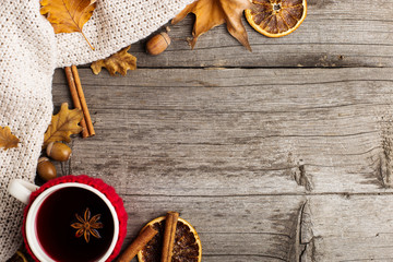 Mulled wine in a cup in a case. Leaves, knitted plaid, dry orange, cinnamon and acorns on the old wooden table, copy space, autumn.