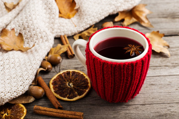Obraz na płótnie Canvas Mulled wine in a cup in a case. Leaves, knitted plaid, dry orange, cinnamon and acorns on the old wooden table, copy space, autumn.