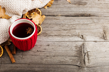 Mulled wine in a cup in a case. Leaves, knitted plaid, dry orange, cinnamon and acorns on the old wooden table, copy space, autumn.