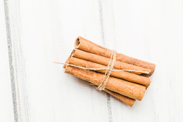 Cinnamon sticks tied up in bundle top view on white wooden background.