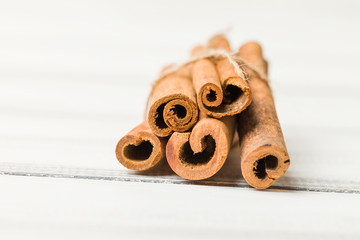 Cinnamon sticks tied up on white wooden background.