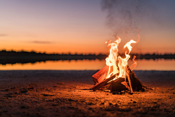Small campfire with gentle flames beside a lake during a glowing sunset. Western Australia,...