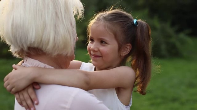 Elegant Caucasian grandmother with stylish hairstyle holding granddaughter in hands. Relatives looking into eyes of each others. Eskimo kiss