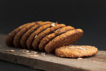 Oatmeal cookies or biscuits with oats, nuts, eggs and flour on brown dark woodenboard with black background, side view.