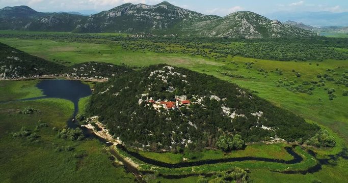 Aerial view of the landscape of Lake Skadar in the mountain and the island with monastery on a beautiful sunny day. Montenegro. The territory of Lake Skadar overgrown with plants.