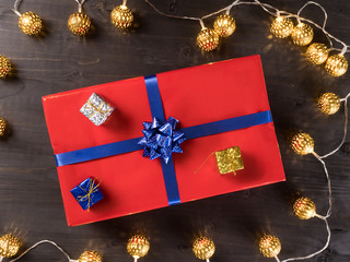 Red christmas gift box with smaller gift boxes on dark wooden floor surrounded by golden lights....