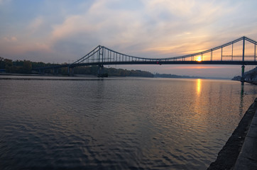 Scenic autumn landscape of Dnipro River and Pedestrian Bridge. The sun is reflected in the water. Selective focus with wide angle lens. Kyiv, Ukraine