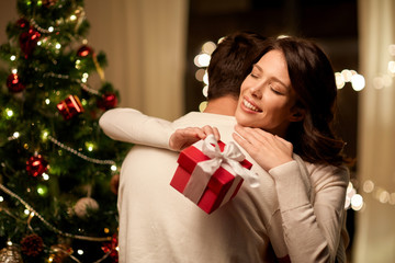 winter holidays and people concept - happy couple with christmas gift hugging at home