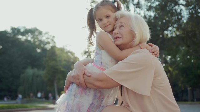 Beautiful Ukrainian litte lady and wonderful grandma hugging in park. Tenderness and love in family. Summertime. Lifestyle. Weekend. Outdoors.