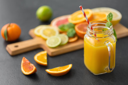 food , healthy eating and vegetarian concept - mason jar glass of orange juice with straw and citrus fruits on slate table top