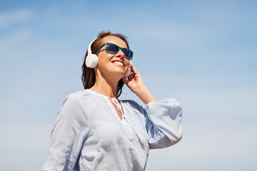 music, people and technology concept - happy smiling woman with headphones over blue sky