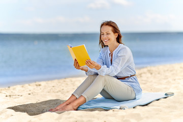 people and leisure concept - happy smiling woman reading book on summer beach
