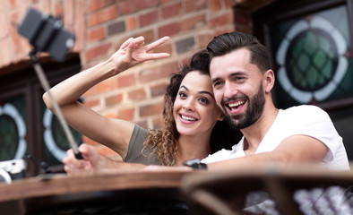 Happy cheerful couple sitting down at a cafe and making selfie