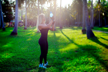 lifestyle. blonde girl at workout drinking water at palm trees.