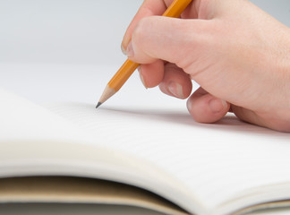 Hand holding a pencil and writing in a notebook.
