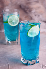 Delicious blue drink with a handful of green lemon. Cocktail with limnom concrete background. Blue cocktail with lemon.