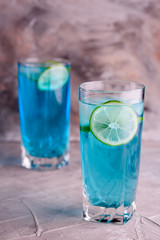 Delicious blue drink with a handful of green lemon. Cocktail with limnom concrete background. Blue cocktail with lemon.