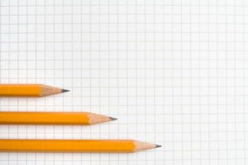 Three pencils lie on a notebook sheet.