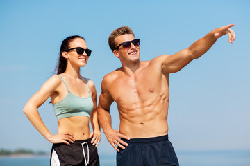 fitness, sport and lifestyle concept - happy couple in sports clothes and sunglasses on beach