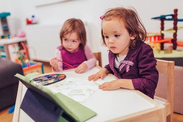 Fototapeta premium Dwie urocze siostrzyczki bawiące się cyfrowym tabletem w domu.
