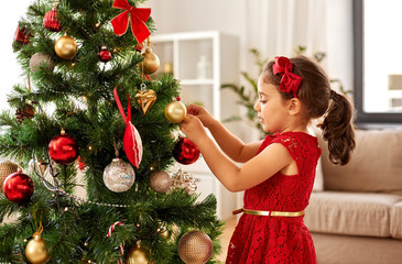 winter holidays and people concept - happy little girl decorating christmas tree at home