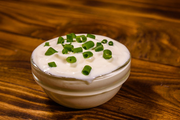 Glass bowl with sour cream and chopped green onion on wooden table