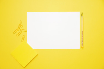 pen white paper yellow stickers and clips on yellow background with copy space top view