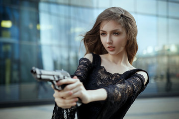 A beautiful elegant girl in an evening dress aims at a  gun.