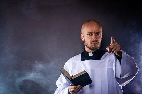 Catholic priest in white surplice and black shirt with cleric collar reading bible