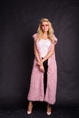 Obraz premium Fashion and people concept - young blonde woman in glasses standing in pink fur coat and smiling