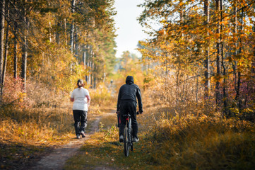 A young woman runs through the woods. The coach is riding a Bicycle nearby. The concept of a...