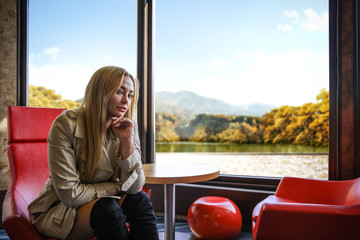 Slim young woman in coat and background of window with autumn landscape. 