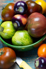 Multicolored assortment of French fresh ripe tomatoes in green bowl on blue wooden table